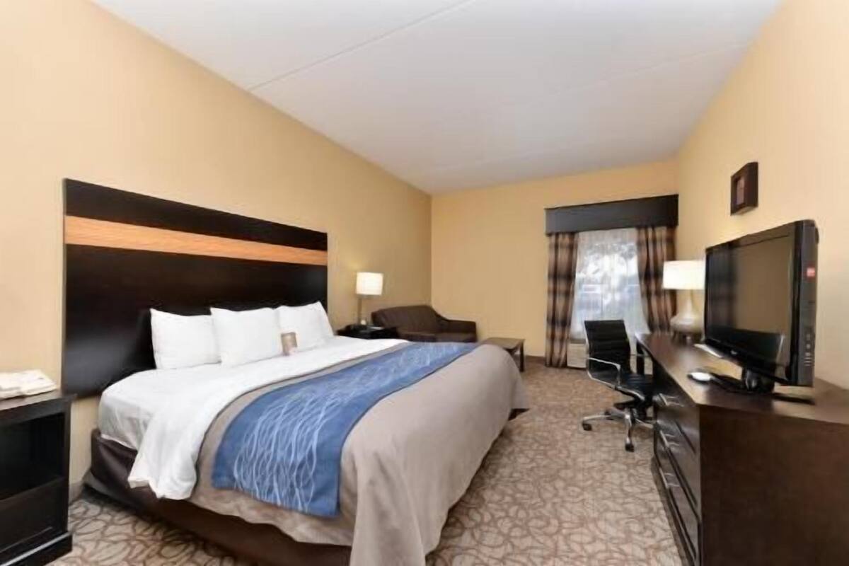 A hotel room with a bed, a desk with a TV, a chair, and a window with curtains.