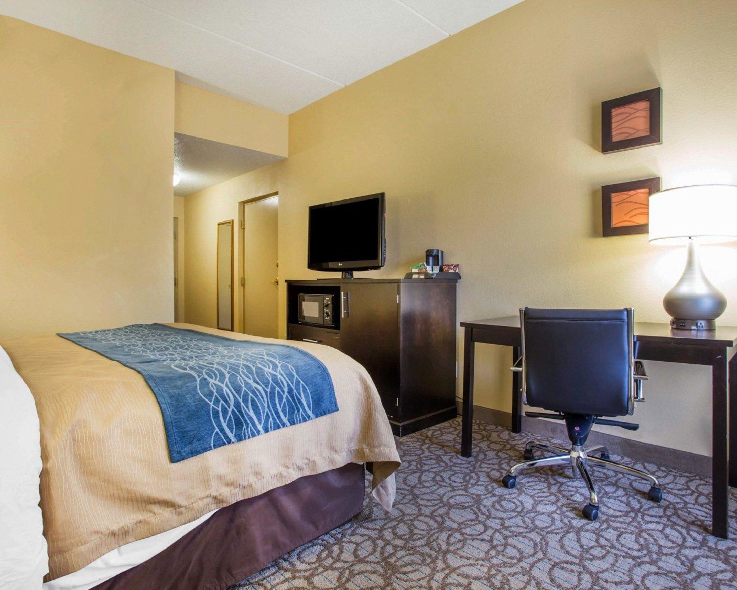 A hotel room with a bed, a desk, a chair, a television, and a lamp.