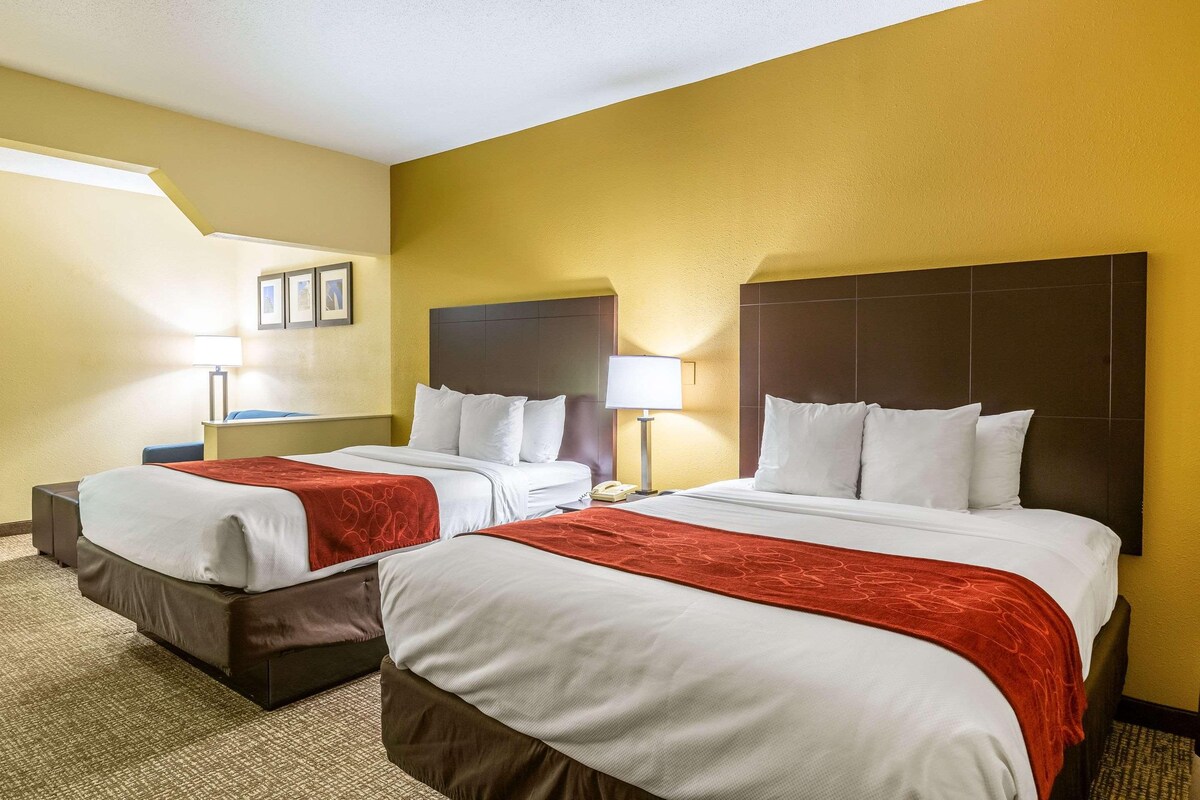A hotel room with two beds, a large window, and a carpeted floor.