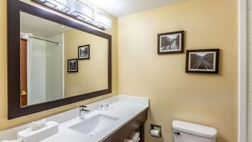 Une salle de bain avec un grand miroir, deux lavabos, des toilettes et des tableaux encadrés accrochés au mur.