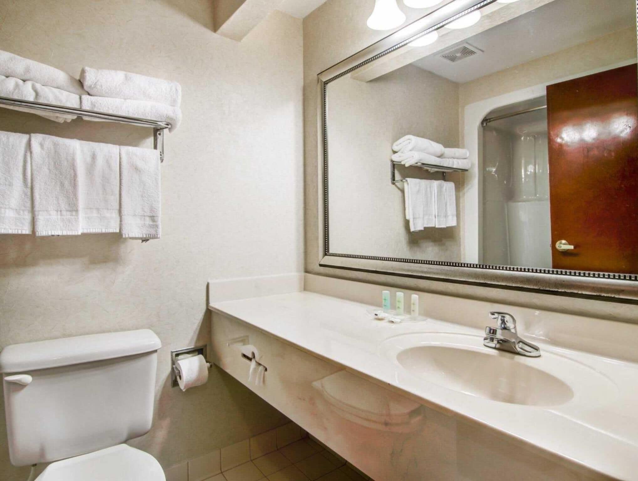 A bathroom with a white sink, a mirror, and a toilet. There are towels hanging on a rack above the toilet.