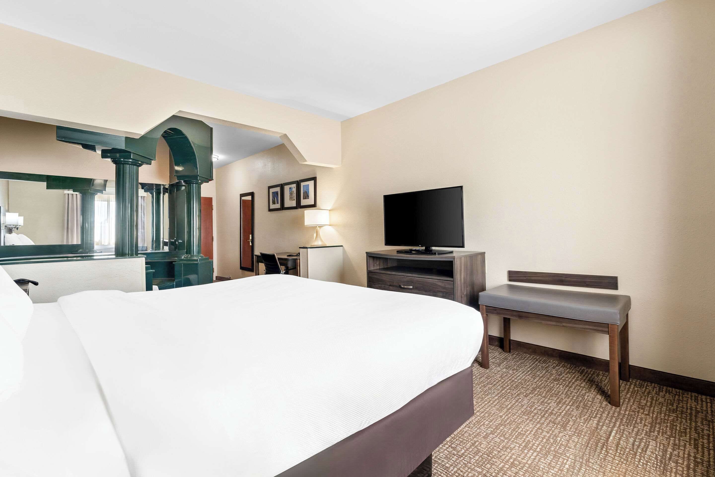 A hotel room with a large bed, a desk, a television, and a bench.