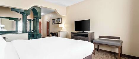 A hotel room with a large bed, a desk, a television, and a bench.