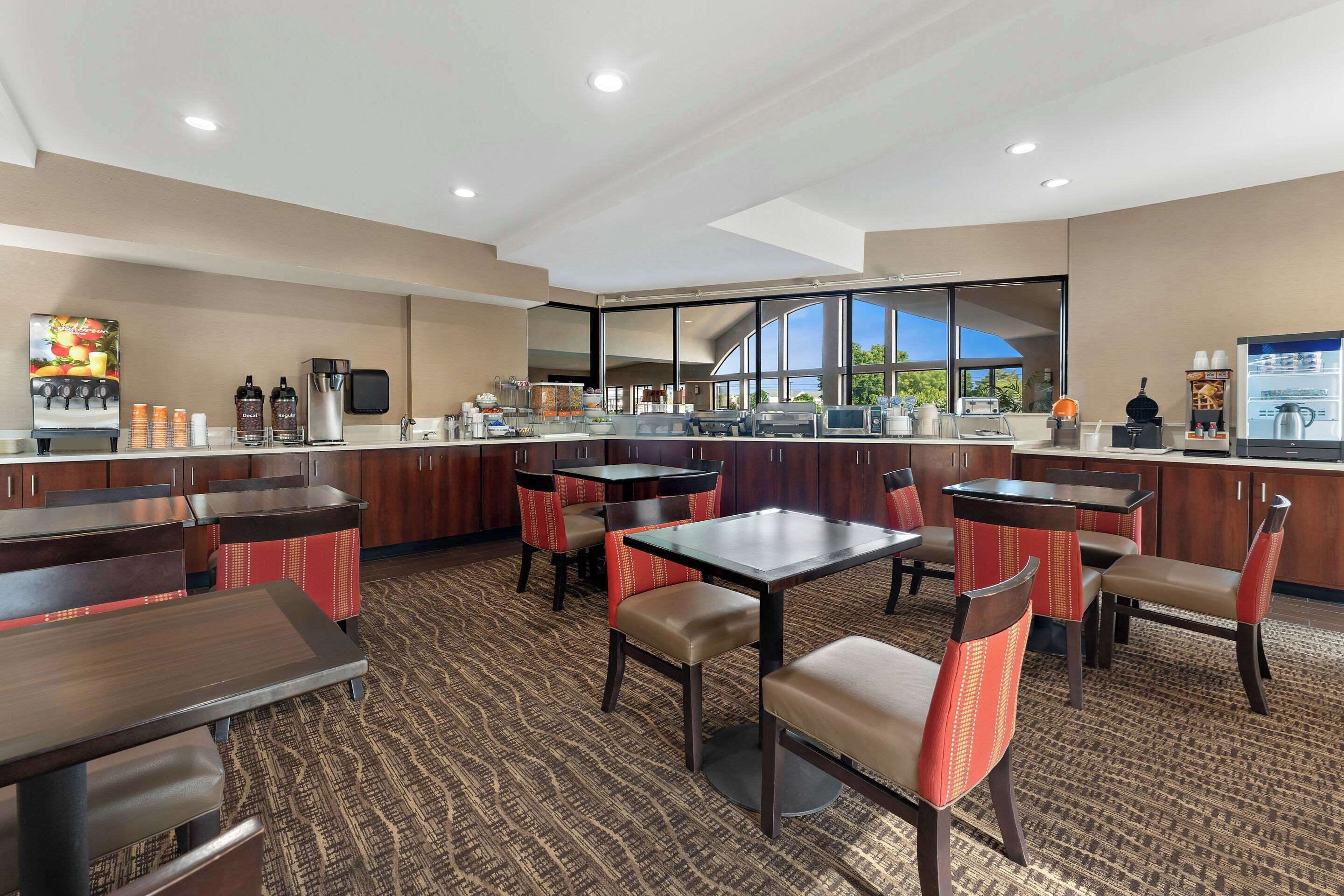 A hotel restaurant with multiple tables and chairs, a coffee machine, and a large window offering a view.
