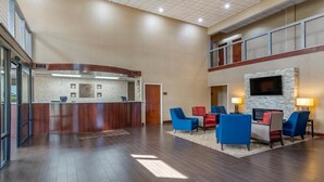 A spacious lobby with a reception desk, seating area, and a TV mounted on a stone wall. - Comfort Suites near Robins Air Force Base (Warner Robins)
