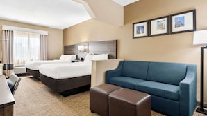A hotel room with two beds, a blue sofa, a brown ottoman, a desk, and a lamp. - Comfort Suites near Robins Air Force Base (Warner Robins)