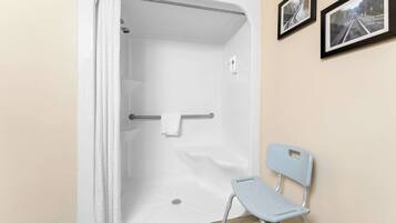 A shower area with a white curtain, a grab bar, and a chair.