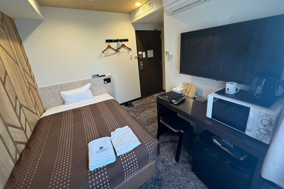 A hotel room with a bed, a desk with a computer, a TV, and a microwave.