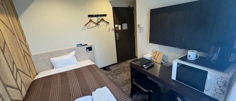 Een hotelkamer met een bed, een bureau met een computer, een televisie en een magnetron.