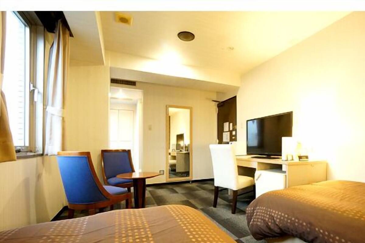 A hotel room with a bed, a desk, a chair, a television, and a window.