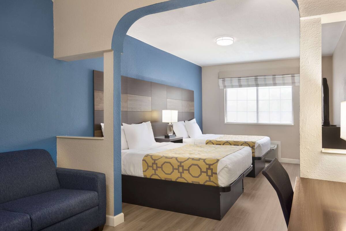 Une chambre d’hôtel avec deux lits, un canapé, un bureau et une fenêtre avec des stores.