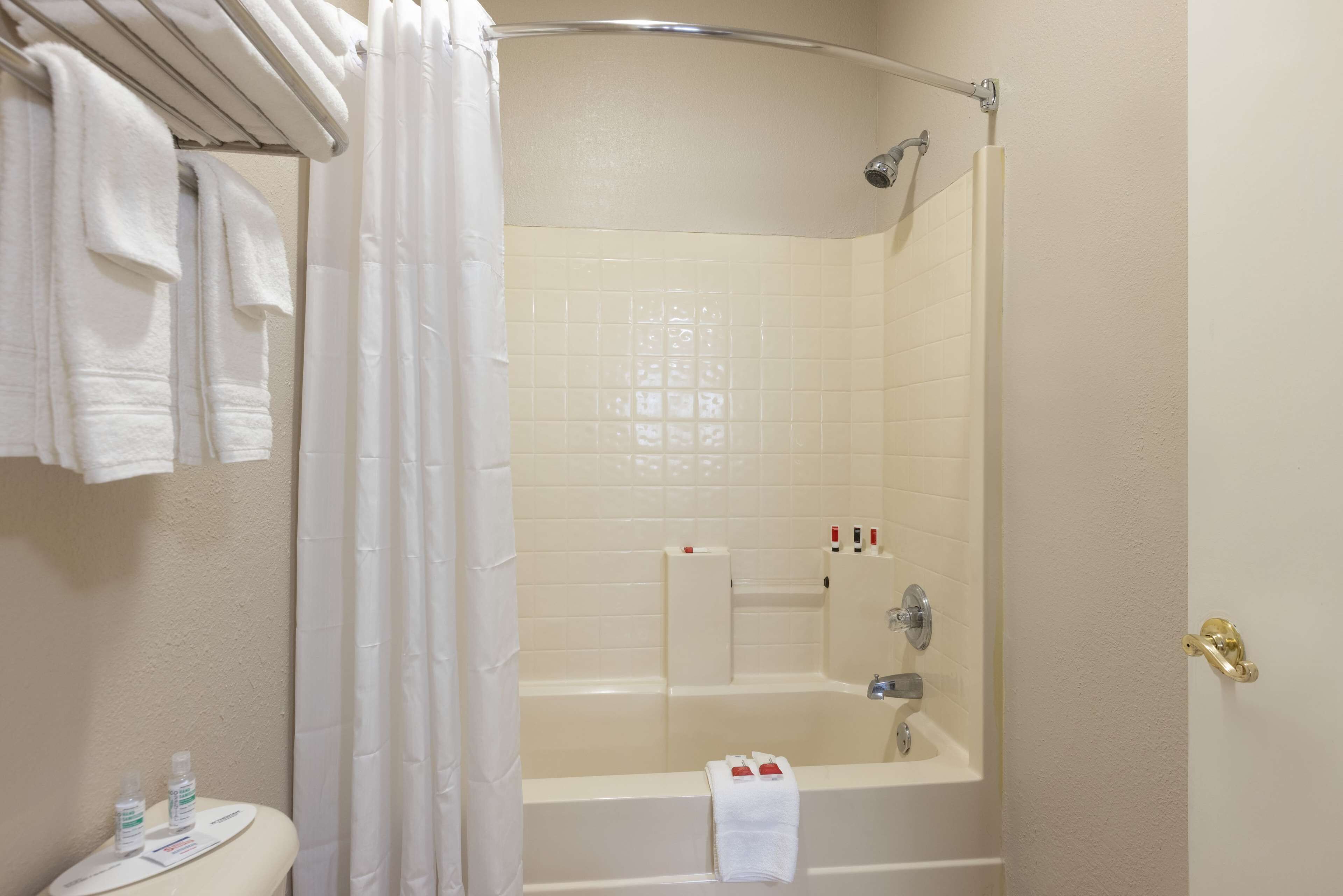 A bathroom with a bathtub, a shower, and a toilet. There are towels hanging on a rack and a bottle of lotion on the counter.