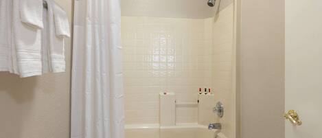 Ein Badezimmer mit Badewanne, Dusche und Toilette. Handtücher hängen an einem Wäscheständer und auf der Ablage steht eine Lotionflasche.
