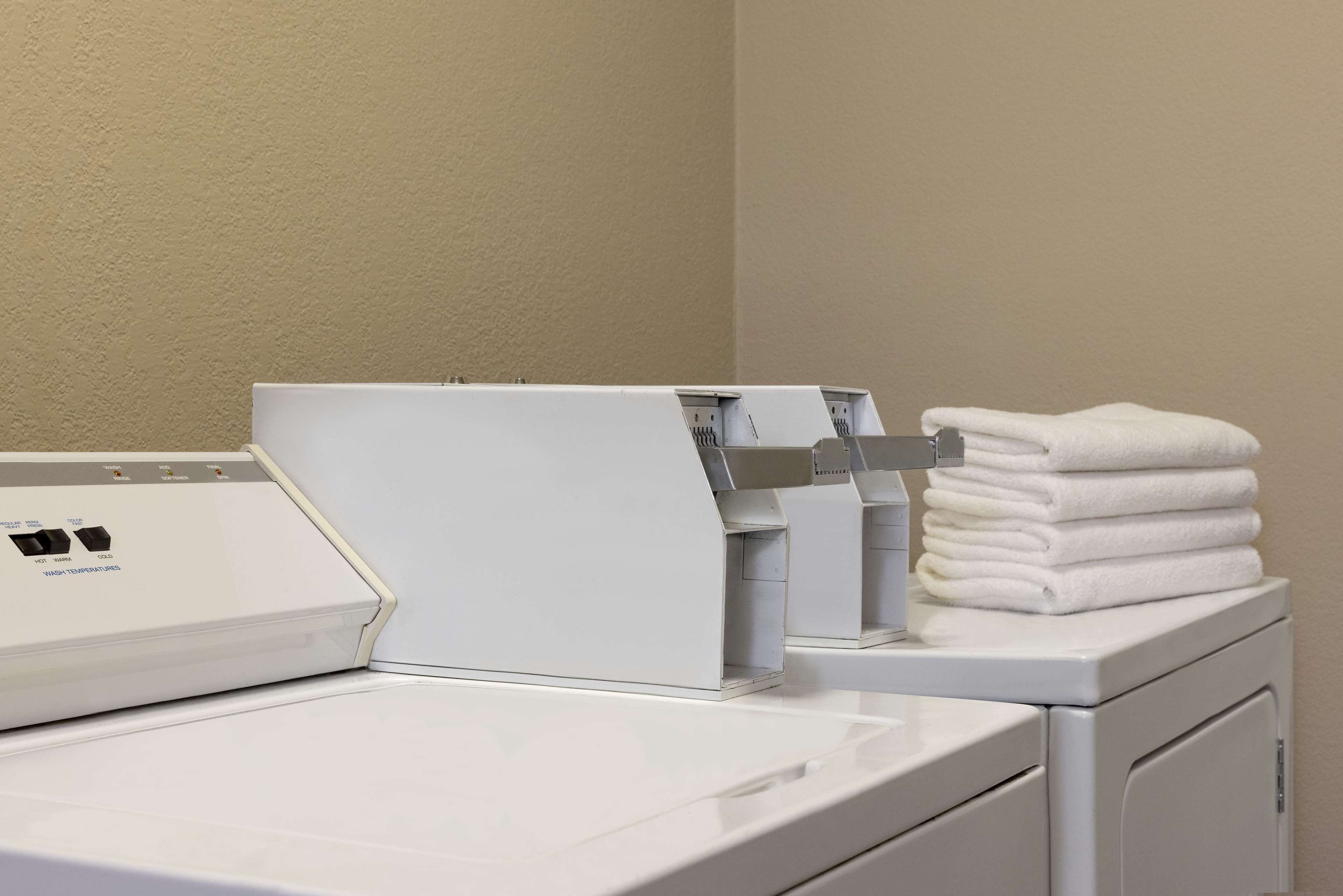 Une machine à laver à chargement frontal, dotée d’un panneau de commande et surmontée d’une pile de serviettes blanches.