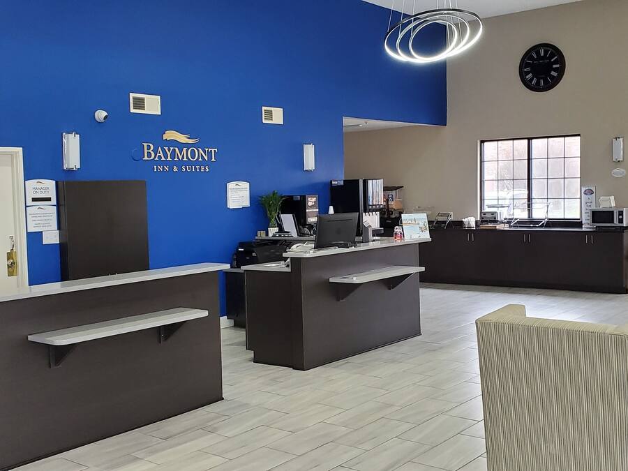 Zona de recepción de un Baymont Inn & Suites, con una pared azul de acento, un reloj y un área de descanso con una mesa de centro y sillas.