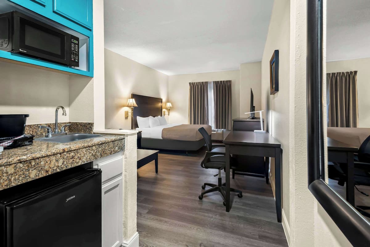 A compact hotel room with a kitchenette, a bed, a desk, and a TV.