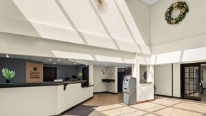Ein Hotel-Empfangsbereich mit einer Rezeption, einem Geldautomaten und einem an der Wand befestigten Kranz.