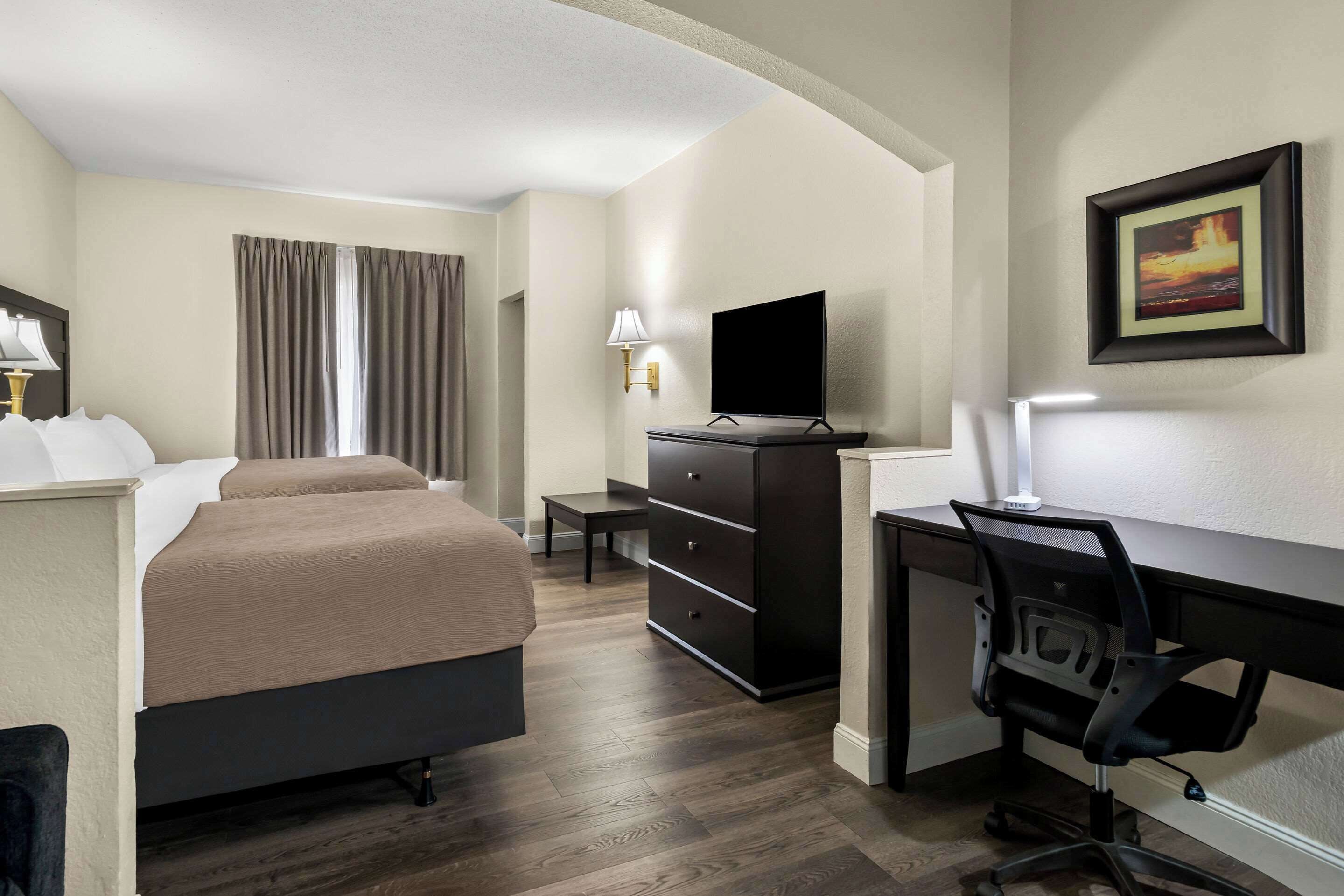 Una habitación de hotel con cama, escritorio, silla, televisor y cómoda.