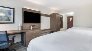 Una habitación de hotel con escritorio, dos camas, televisor y armario.