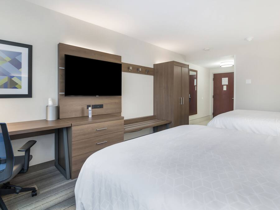 Una habitación de hotel con escritorio, dos camas, televisor y armario.