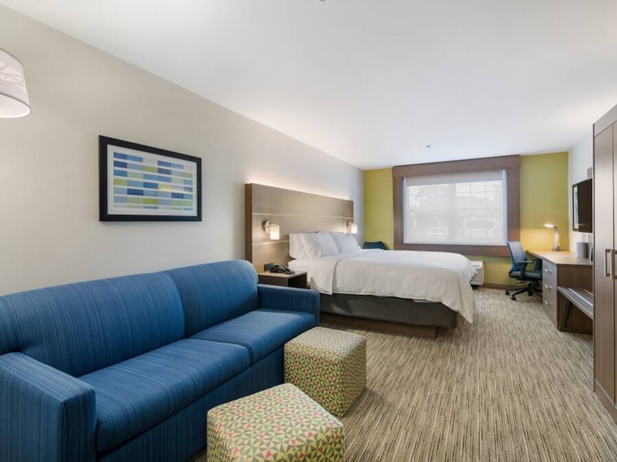 A hotel room with a blue sofa, a bed, a desk, and a large window.