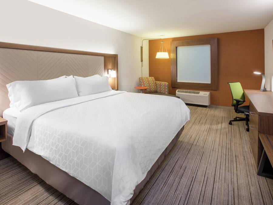 A hotel room with a large bed, a desk, a chair, a TV, and a wall-mounted heater.