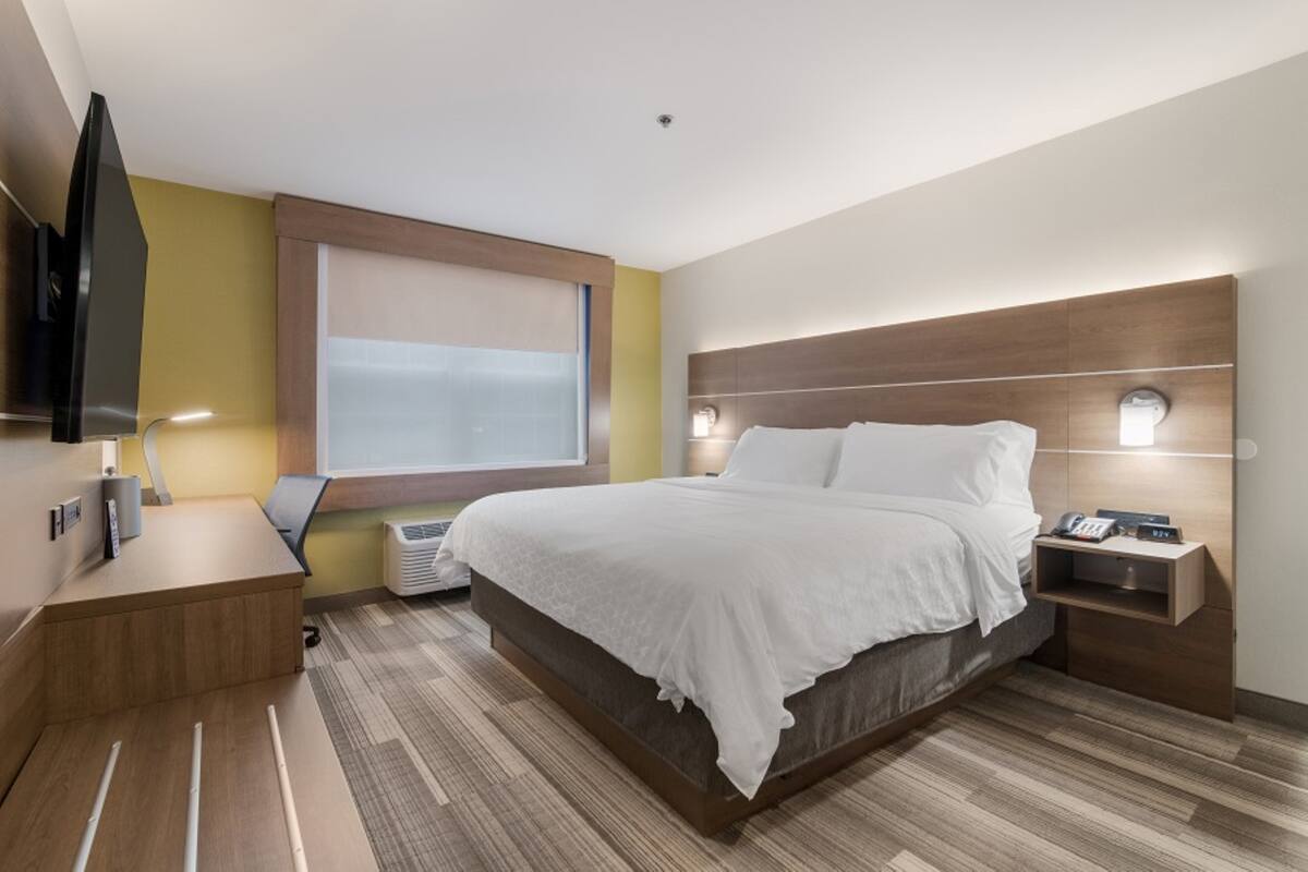A modern hotel room with a large bed, bedside tables, a flat-screen TV, and a window with blinds.