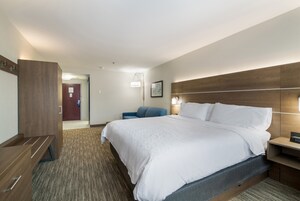 A hotel room with a large bed, a desk, a chair, and a wardrobe.