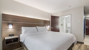 A hotel room with a large bed, a nightstand, a wooden headboard, and a mirror above the door.