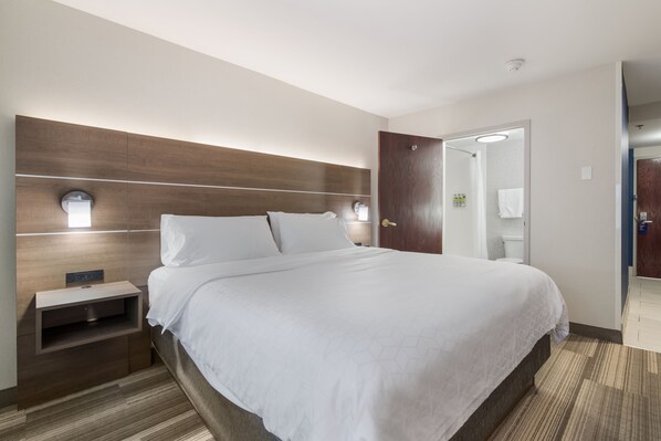 Habitación de hotel con una cama grande, una mesita de noche, cabecera de madera y un espejo sobre la puerta.