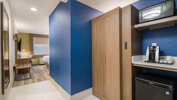 A compact hotel room with a kitchenette, a bed, and a small seating area.