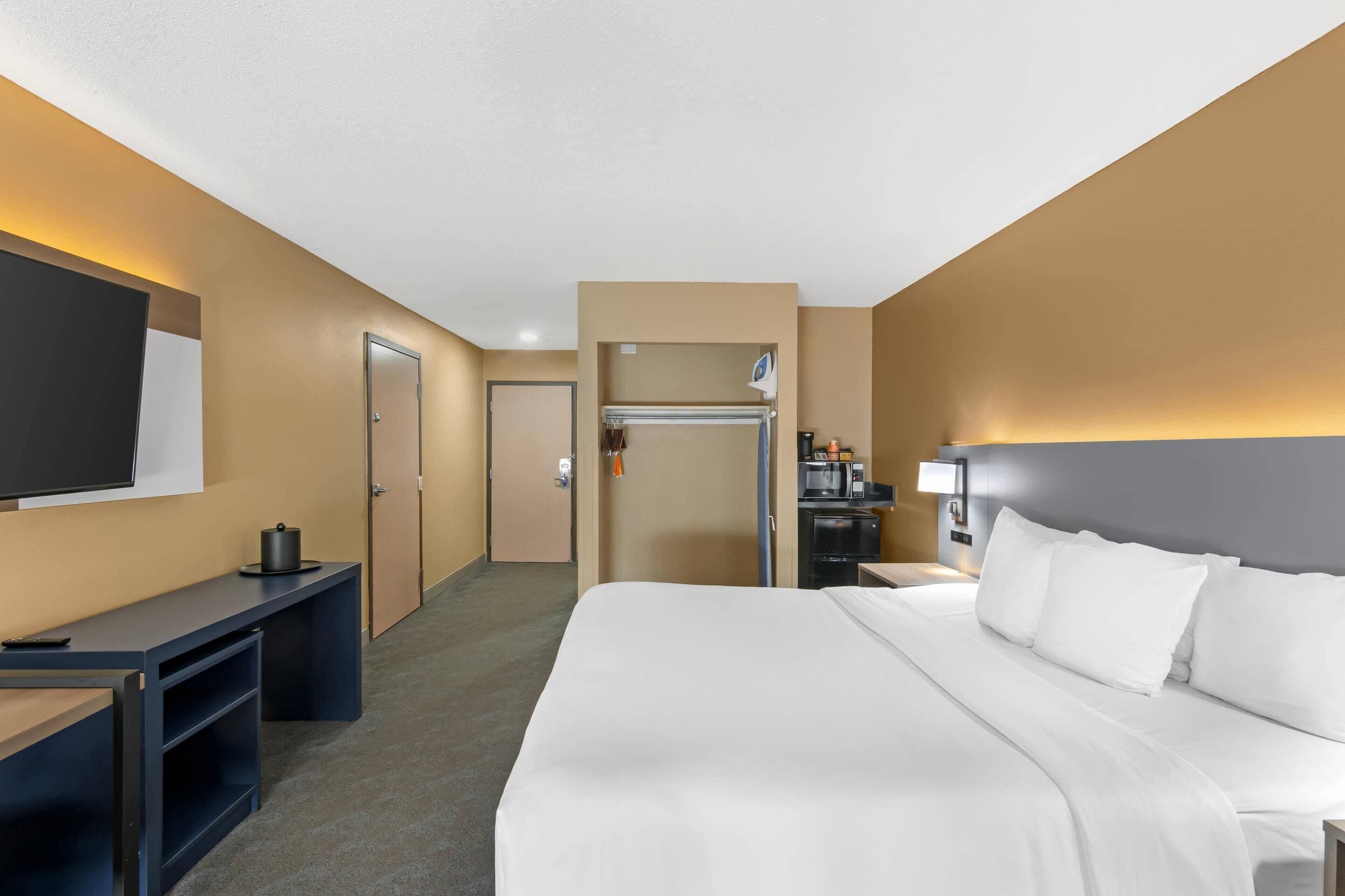 A hotel room with a bed, a desk, a TV, a wardrobe, and a kitchenette.