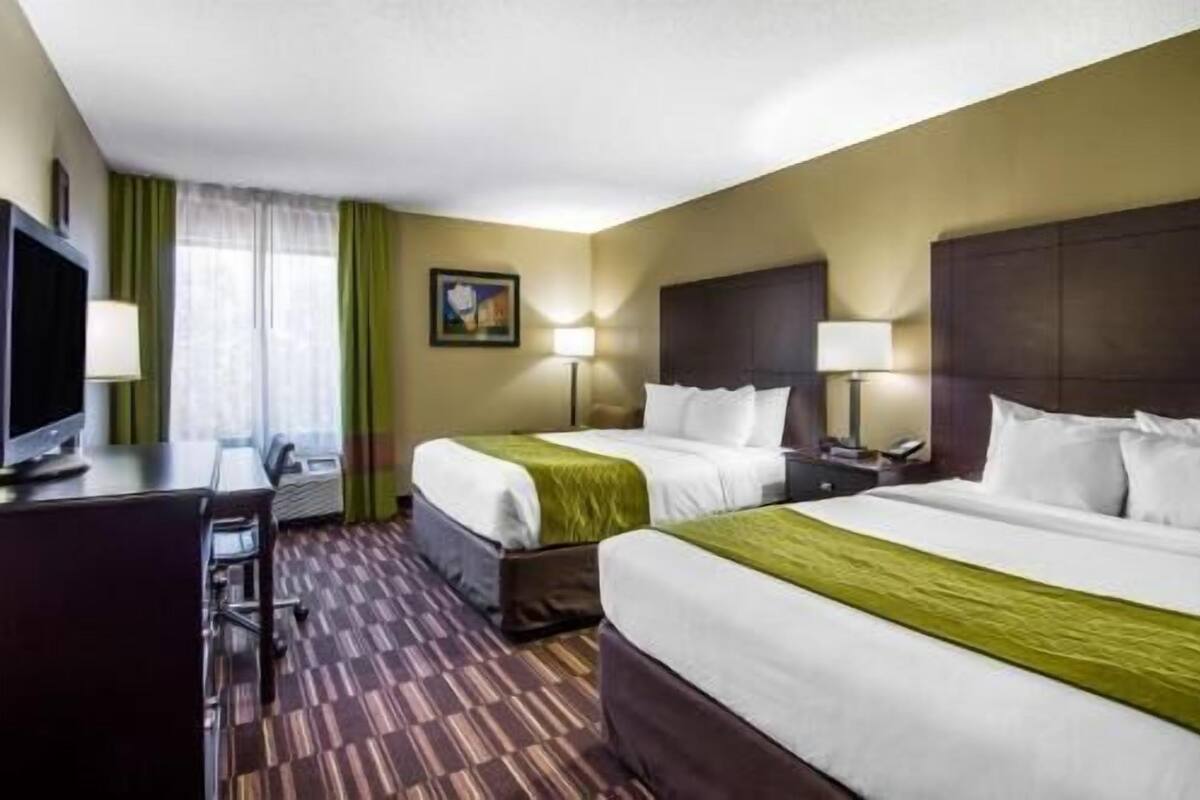 Quarto de hotel com duas camas, uma escrivaninha, televisão e um quadro na parede.