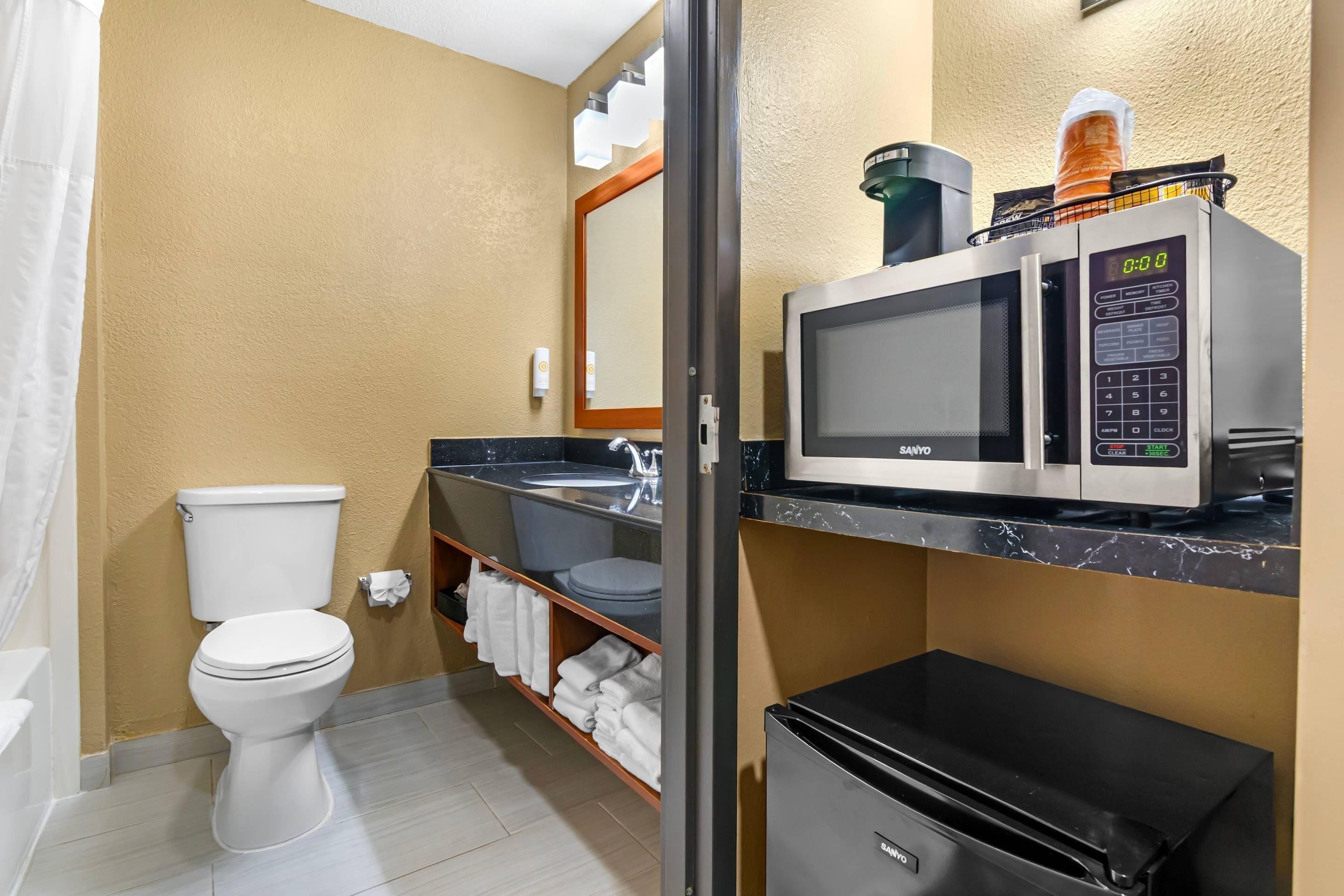 A compact bathroom with a toilet, a microwave, and a small refrigerator.