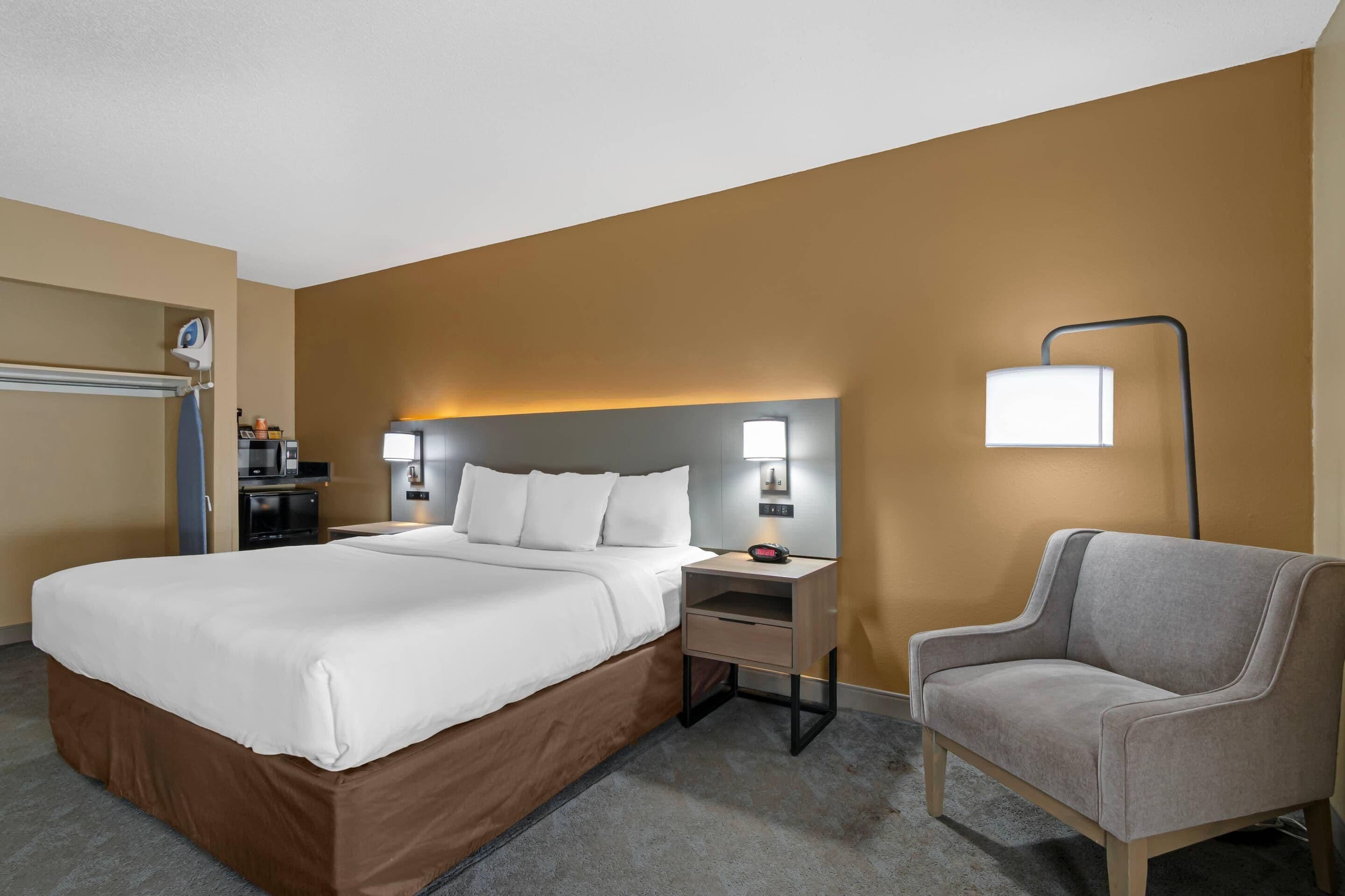 A hotel room with a large bed, bedside tables, a chair, and a desk with a lamp.