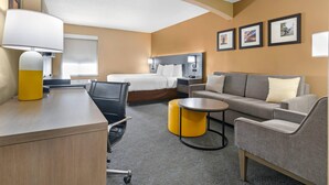 A hotel room with a bed, a sofa, a desk with a lamp, a chair, and a small table. - Comfort Inn & Suites Kansas City - Northeast (Kansas City)