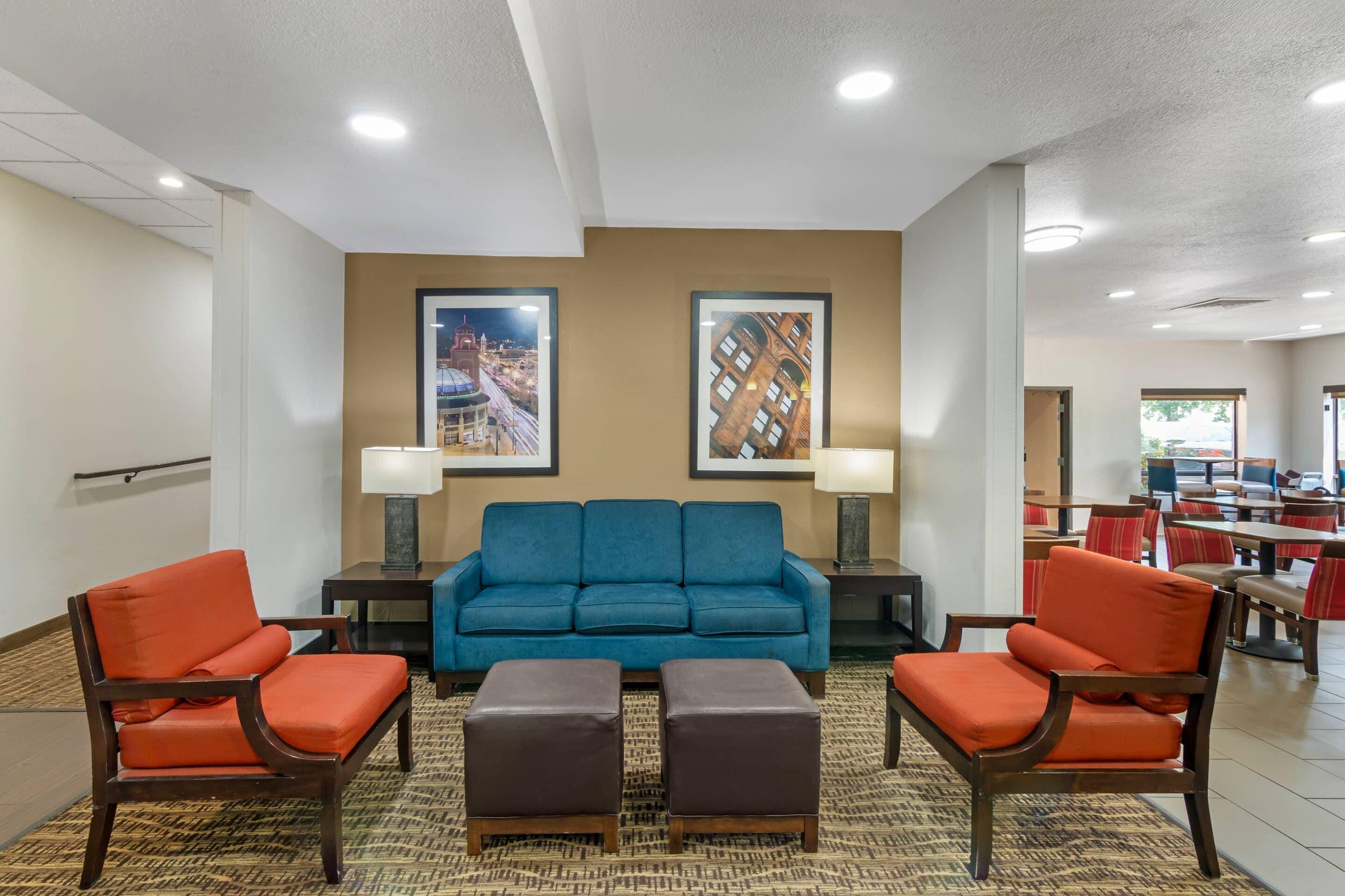 A hotel lobby with a blue sofa, orange chairs, a patterned carpet, and framed pictures on the wall.