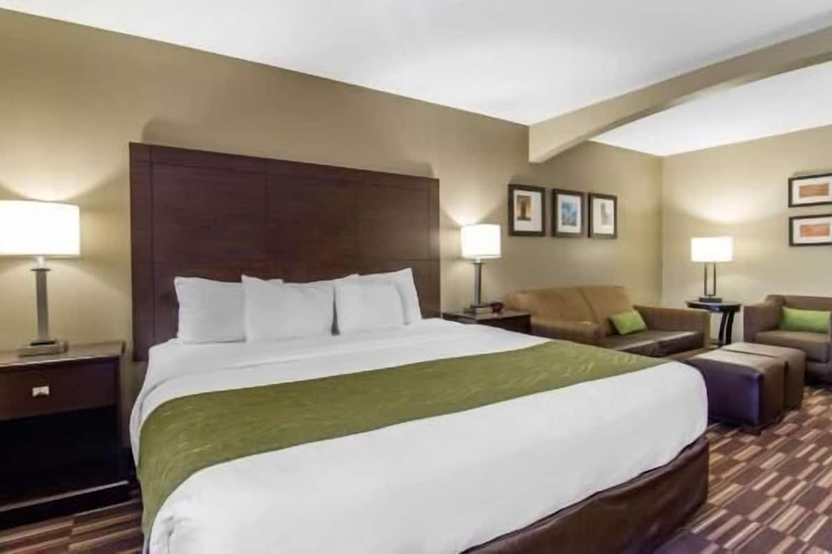 Quarto de hotel com uma cama grande, duas mesas de cabeceira, uma cadeira, um sofá e quadros nas paredes.