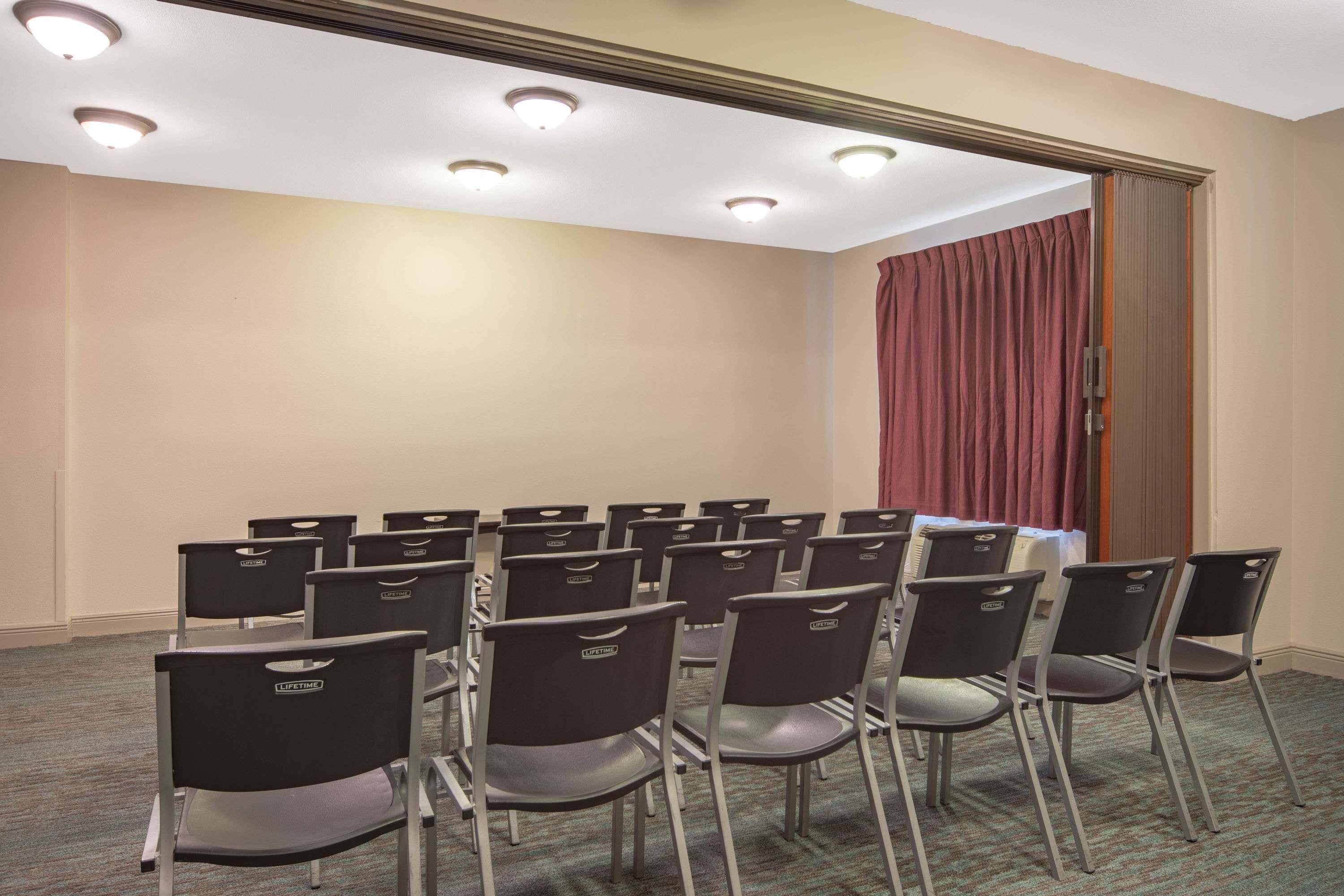 A conference room with rows of chairs, a carpeted floor, and a door with a curtain.