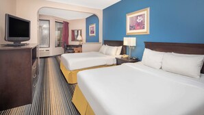 Habitación de hotel con dos camas, televisión, escritorio y baño visible a través de un arco.
