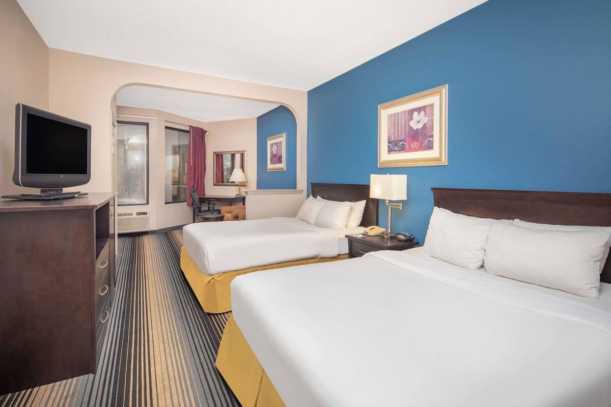 Habitación de hotel con dos camas, televisión, escritorio y baño visible a través de un arco.