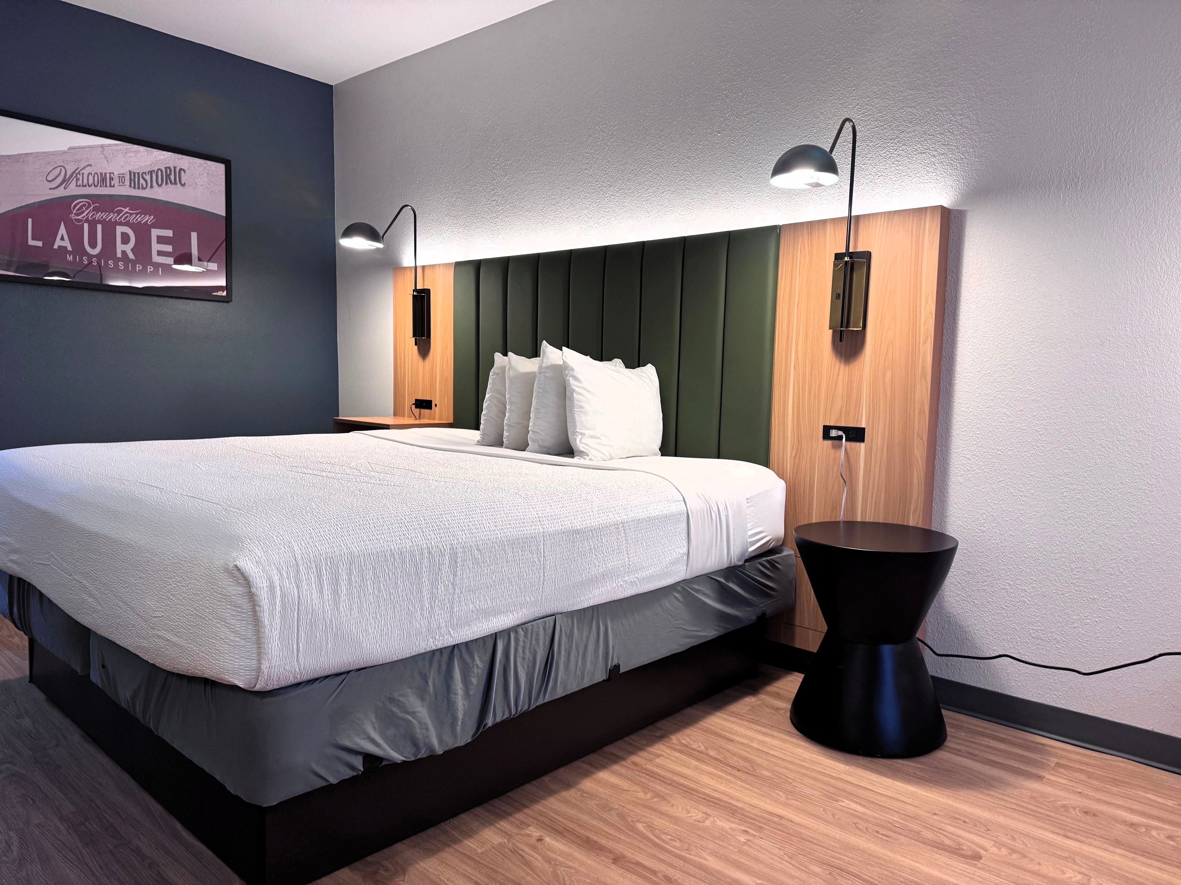 Una habitación de hotel moderna con una cama grande, dos mesitas de noche, un televisor de pared y una lámpara negra original.