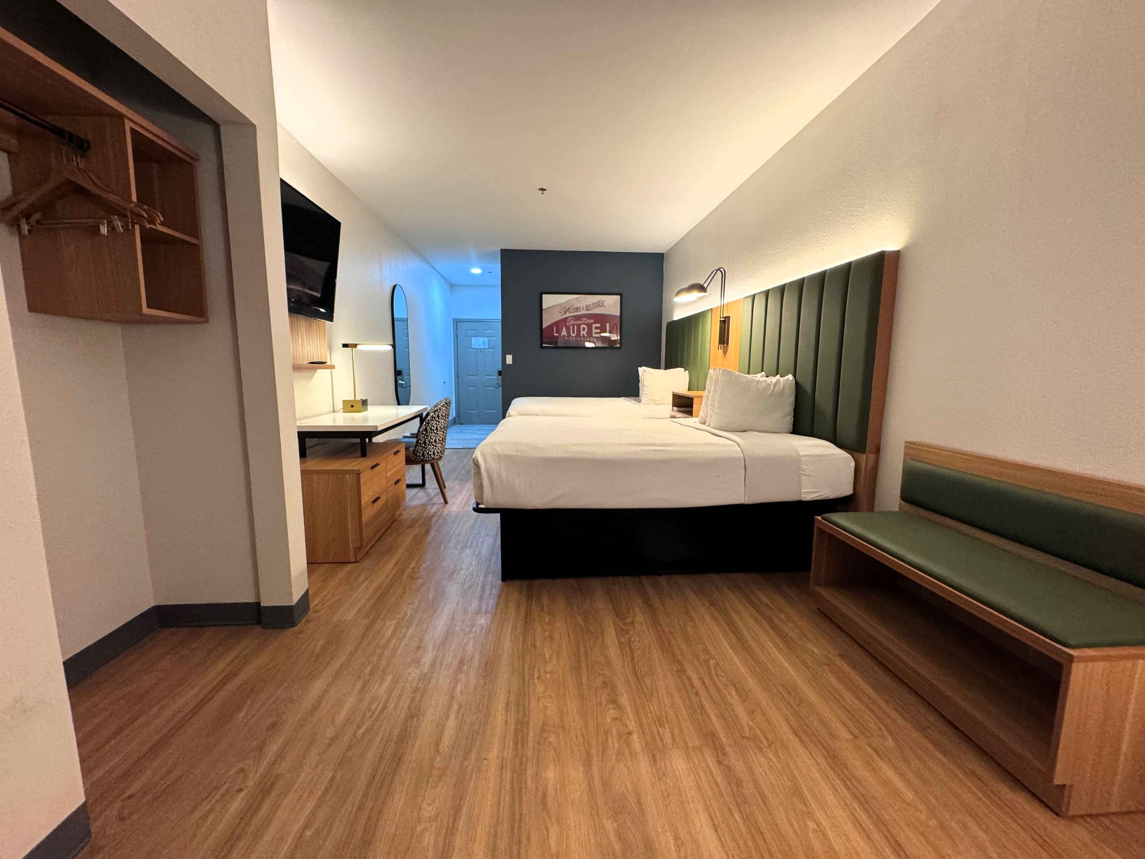 A hotel room with a bed, desk, chair, and a bench.