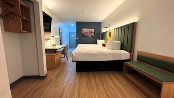 A hotel room with a bed, desk, chair, and a bench.