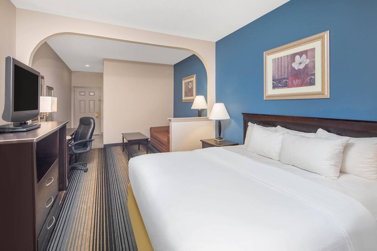 Habitación de hotel con una cama grande, un escritorio con computadora, una silla, una lámpara y un televisor.