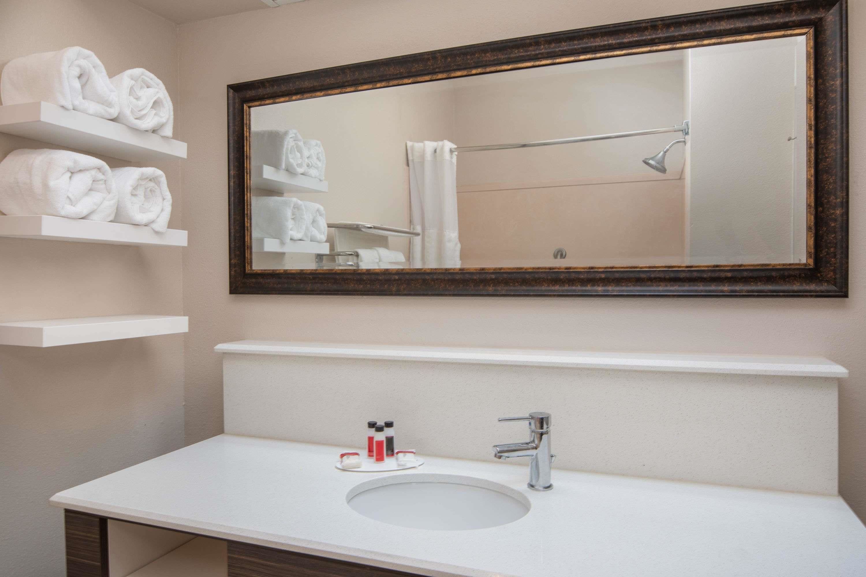 Une salle de bain avec un lavabo blanc, un miroir avec un cadre en bois et des étagères où sont pliées des serviettes.