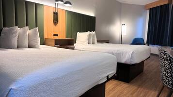 A hotel room with two beds, a wooden headboard, a bedside table, a chair, and a large window with curtains.