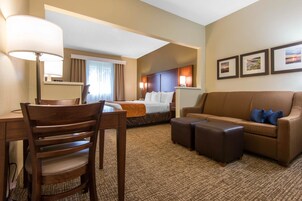 Quarto de hotel com uma cama, uma escrivaninha com cadeira, um sofá e uma mesa de centro. Há três quadros na parede.