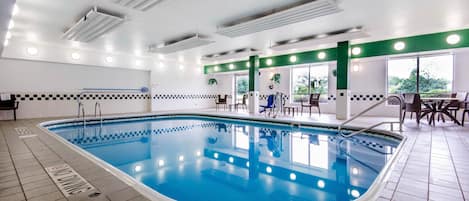 An indoor swimming pool with a checkered border, a tiled floor, and a seating area with tables and chairs.