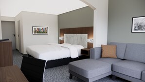 A modern hotel room with a bed, a grey sofa, a wooden desk, and a cityscape picture on the wall. - Quality Suites Austin South St. Elmo District (Austin)